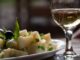A dish of potato with green onion and glass of wine