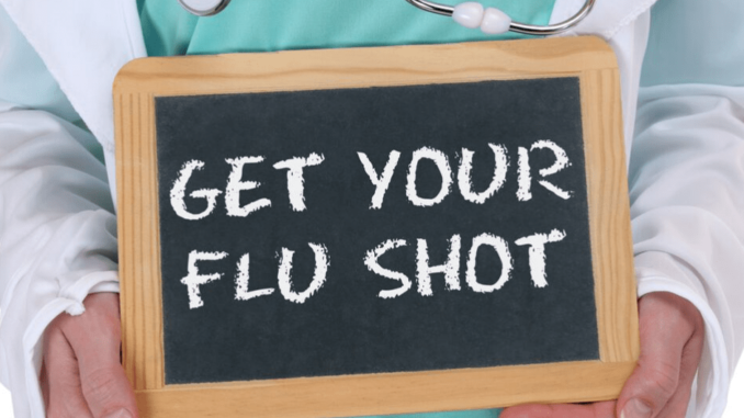 A doctor holding a board with "get your flu shot"
