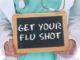 A doctor holding a board with "get your flu shot"