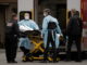 4 people standing nearly ambulance, moving medical stretcher
