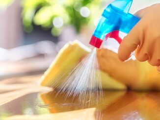 A person wearing yellow gloves spraying cleaning liquid on the table