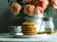 A table with a dish of cookies, tea and bottle of flowers